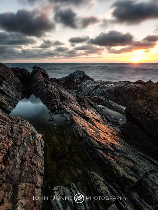 The sun is just above the horizon sending soft light upon the rocks of Greystones beach in Co. Wicklow, Ireland The sun is just above the horizon sending soft light upon the rocks of Greystones beach in Co. Wicklow, Ireland by John Dunne.