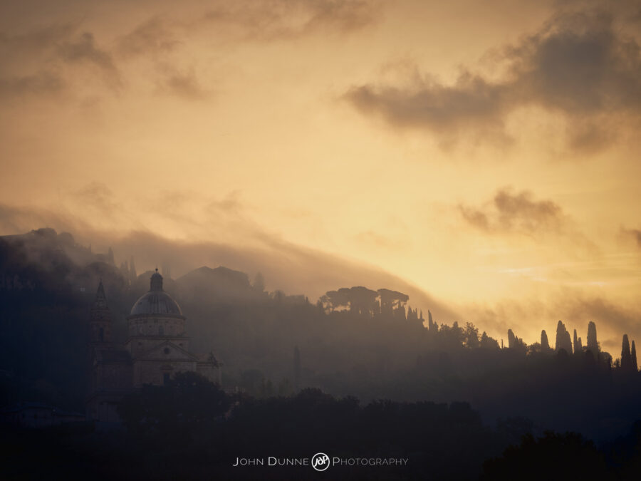 The sun rises over San Biaggio Church in Montepulciano in Italy, casting a warm glow amongst the low lying clouds.